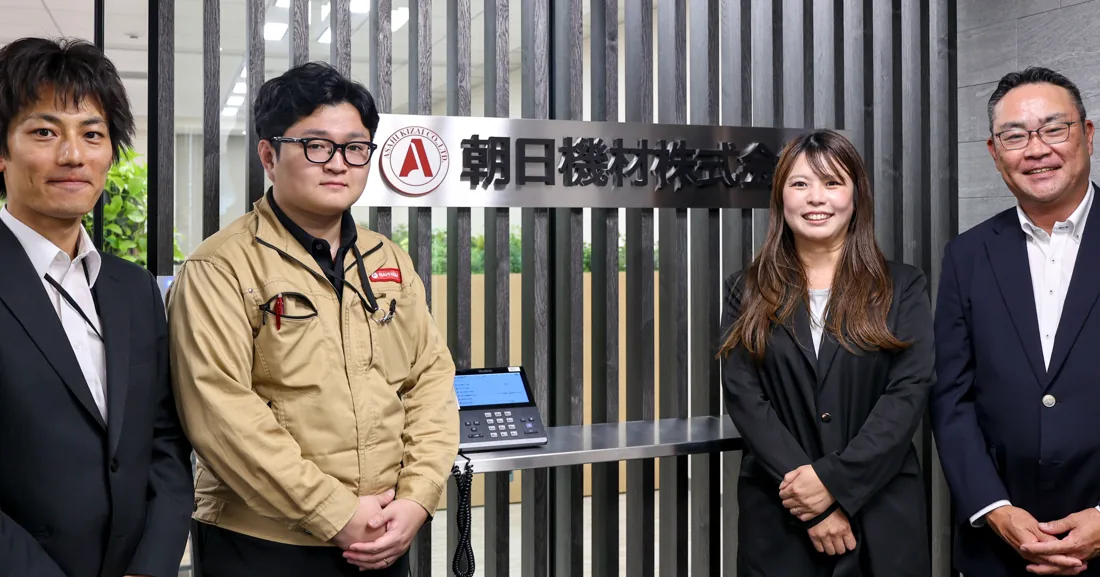 朝日機材株式会社の社名サインの前に並ぶ4名の担当者の写真