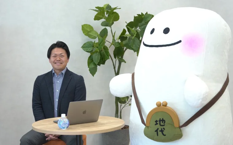 Mr. Shoichi Yamazaki, General Manager of the Third Sales Department at Sansei Landic Co., Ltd., is pictured sitting in front of a laptop alongside the company’s mascot, “Sokochi-kun.”