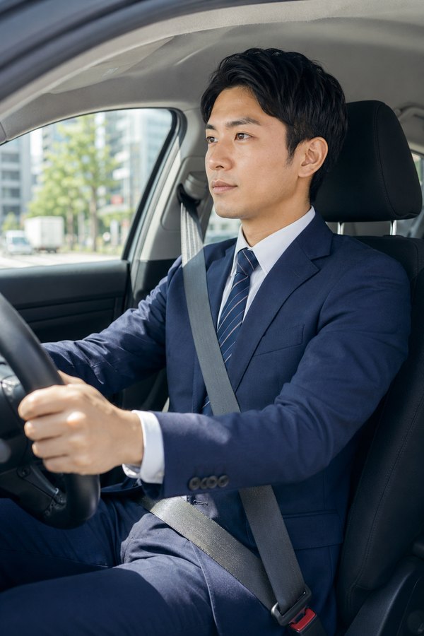 社用車の運転席でシートベルトを着用し運転する営業担当者